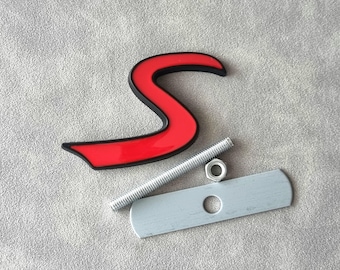 May include: Red plastic letter "S" with a black outline, a silver screw, a silver nut, and a silver metal plate with a hole in the center.