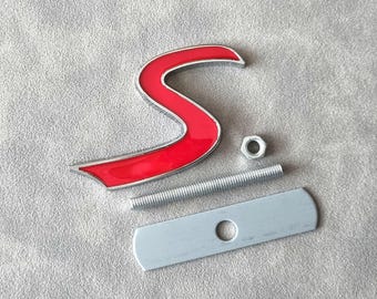 May include: A red metal 'S' logo with a silver mounting bracket, nut, and bolt.