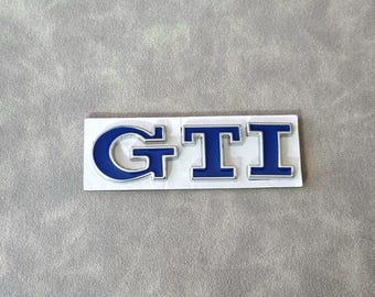 May include: A silver and blue "GTI" emblem with a white background.