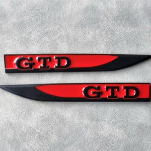以下が含まれることがあります： 「GTD」という黒い文字が書かれた、黒と赤の車のエンブレムが2つあります。