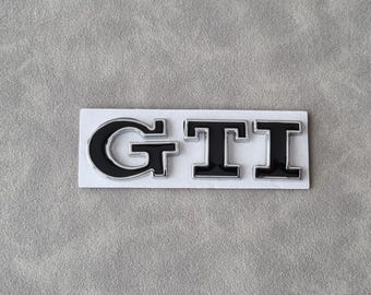 May include: Black and silver GTI emblem with a white background.