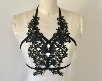 May include: Black lace bralette with adjustable straps and floral detailing. The bralette is on a white mannequin.