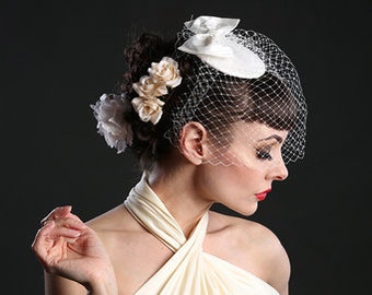 Puede incluir: Un vestido blanco de tirantes con escote drapeado y un velo de jaula de pájaro blanco con un pequeño sombrero blanco y adornos florales.