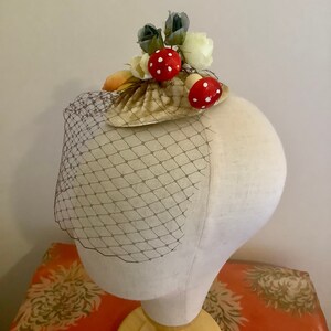 Puede incluir: Una concha blanca y marr&oacute;n con detalles de setas rojas y blancas y flores blancas y grises. La concha est&aacute; sobre un velo de red marr&oacute;n.