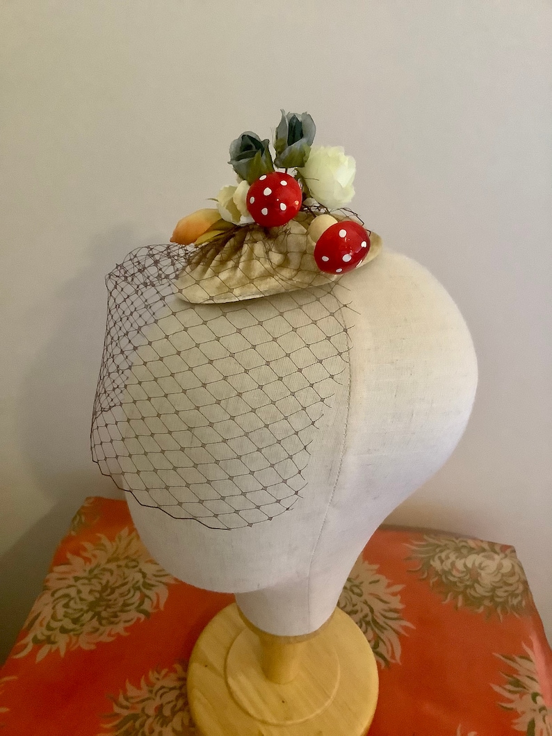 Puede incluir: Una concha blanca y marr&oacute;n con detalles de setas rojas y blancas y flores blancas y grises. La concha est&aacute; sobre un velo de red marr&oacute;n.