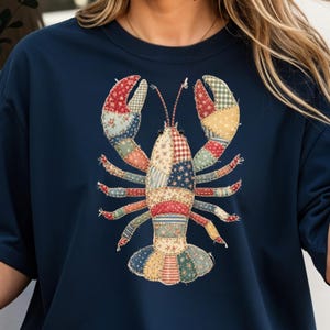 Könnte beinhalten: Marineblaues Sweatshirt mit einem Patchwork-Hummer-Design. Der Hummer besteht aus verschiedenen Stoffmustern in Rot, Blau, Gelb und Grün. Das Design ist auf der Vorderseite des Shirts zentriert und schafft ein maritimes Thema.
