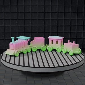 以下が含まれることがあります： ピンク、緑、青のパステルカラーの4両編成の玩具列車セット。列車は白と黒のストライプが入った丸いプラットフォームに展示されています。背景は暗く、質感のある表面です。