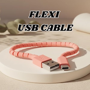 以下が含まれることがあります： USB-AとUSB-Cコネクタを備えた、柔軟なコーラルカラーのUSBケーブル。コイル状のケーブルは白い円形のプラットフォーム上にあります。「FLEXI USB CABLE」というテキストがケーブルの上に白黒で表示されています。