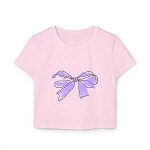 May include: A pink cropped t-shirt with a purple bow drawn on the front.