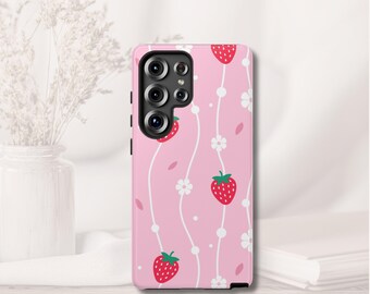 May include: Pink phone case with a repeating pattern of red strawberries, white flowers, and white dotted lines. The case has a black camera module and black side buttons. The background is a light pink color.
