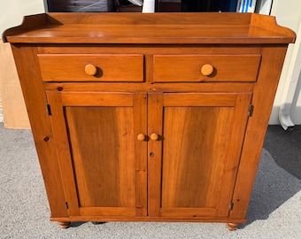 May include: A wooden cabinet with two drawers and two doors. The cabinet is a light brown color and has a simple design. It has a top surface that is slightly curved.