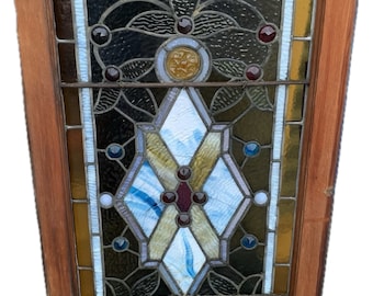 May include: A stained glass window with a geometric design featuring blue, white, brown, and red glass pieces. The window is framed in wood.