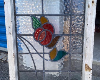 May include: A rectangular stained glass window with a white, distressed wooden frame. The window features a floral design with red, yellow, green, and brown glass pieces. The glass has a textured, rippled appearance.