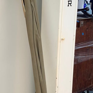 May include: A white metal cabinet labeled "STRETCHER" with a green canvas stretcher with wooden poles stored inside. The stretcher is hanging on the wall with a number "10" plaque.