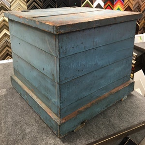 K&ouml;nnte beinhalten: Eine antike Holzkiste mit blauer Lackierung. Die Kiste hat einen Deckel mit Scharnieren und einen Sockel mit leicht erh&ouml;htem Rand. Die Kiste besteht aus Holzbrettern und hat ein rustikales, verwittertes Aussehen.