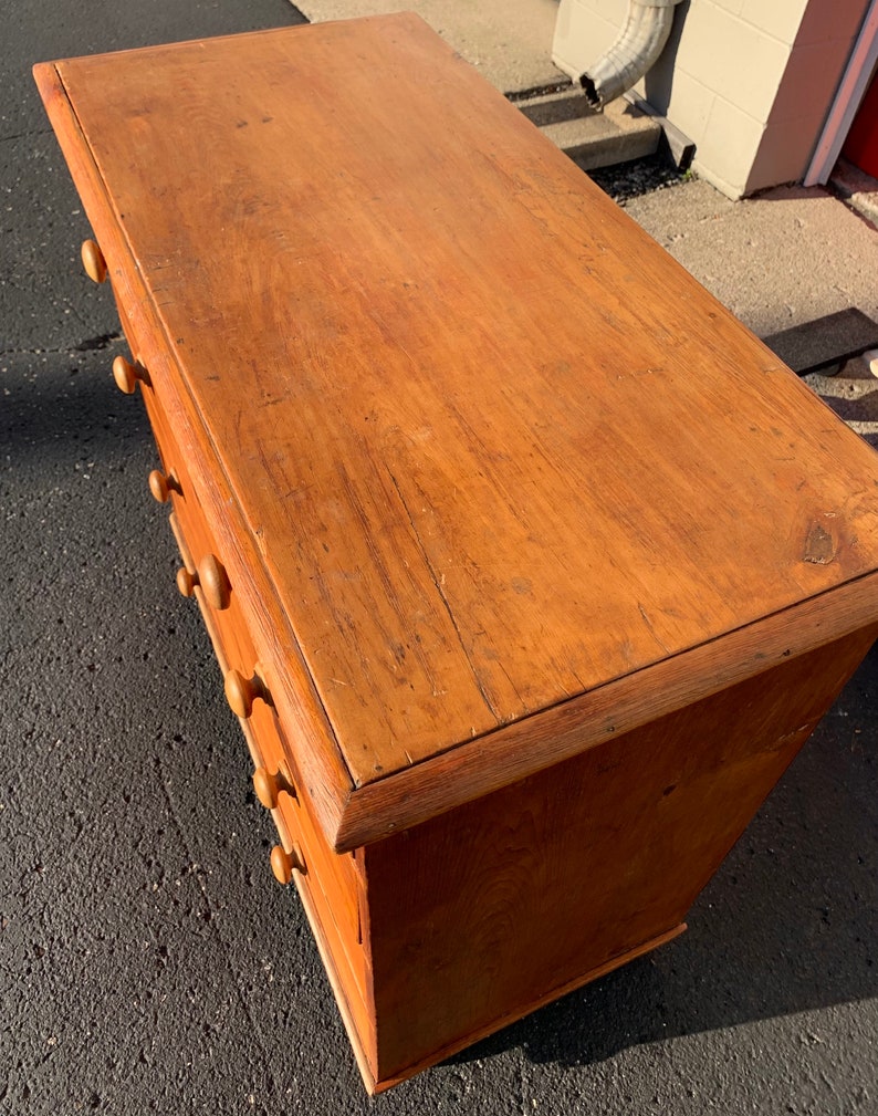 May include: A wooden chest of drawers with a light brown finish and six drawers. The drawers have wooden knobs. The chest is sitting on a black surface.