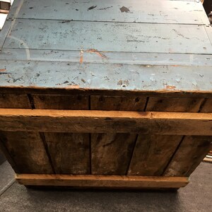 K&ouml;nnte beinhalten: Eine antike Holzkiste mit einem blau gestrichenen Deckel. Die Kiste hat ein rustikales Aussehen mit sichtbarer Holzmaserung und Gebrauchsspuren. Die Kiste ist offen und das Innere ist sichtbar.