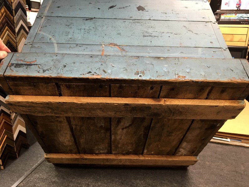 K&ouml;nnte beinhalten: Eine antike Holzkiste mit einem blau gestrichenen Deckel. Die Kiste hat ein rustikales Aussehen mit sichtbarer Holzmaserung und Gebrauchsspuren. Die Kiste ist offen und das Innere ist sichtbar.