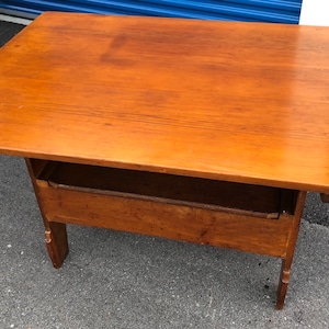 May include: A wooden table with a drawer and a drop-leaf design. The table is made of light brown wood and has a natural finish.