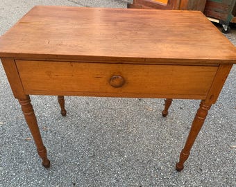 May include: A wooden table with a single drawer and turned legs. The table is made of light wood and has a simple, rustic design.