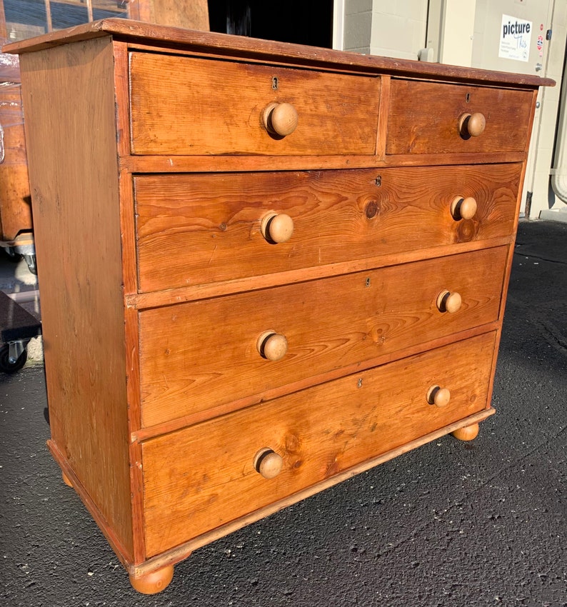 May include: A five-drawer wooden chest of drawers with a light brown finish. The drawers have wooden knobs and are numbered 1 through 5.