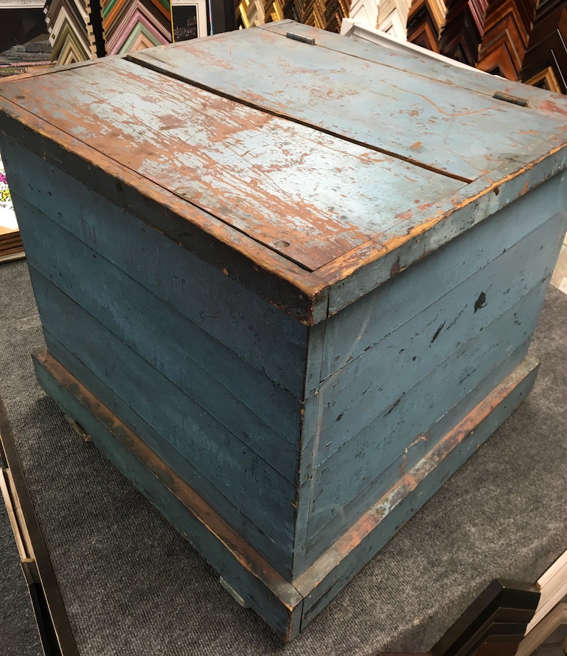 K&ouml;nnte beinhalten: Eine antike Holzkiste mit einem Scharnierdeckel. Die Kiste ist in einem verblassten Blau gestrichen und hat ein abgenutztes, rustikales Aussehen. Die Kiste besteht aus Holzbrettern und hat eine einfache, rechteckige Form.