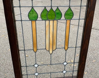 May include: A stained glass window with a wood frame. The glass features a design of four stylized green leaves with yellow and white accents.