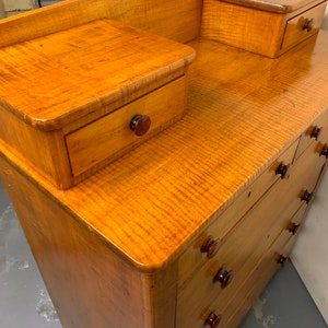 Pode incluir: C&ocirc;moda de madeira vintage com acabamento castanho claro. A c&ocirc;moda possui v&aacute;rias gavetas com puxadores castanhos escuros e dois pequenos arm&aacute;rios laterais. O veio da madeira &eacute; vis&iacute;vel e a pe&ccedil;a tem um acabamento brilhante.