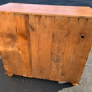 May include: The back of a wooden cabinet with a light brown finish. The cabinet has a simple design with a few visible wood grain patterns. The cabinet has a few small holes and scratches on the surface.