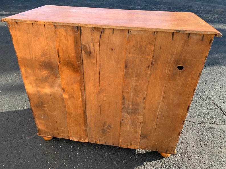 May include: The back of a wooden cabinet with a light brown finish. The cabinet has a simple design with a few visible wood grain patterns. The cabinet has a few small holes and scratches on the surface.
