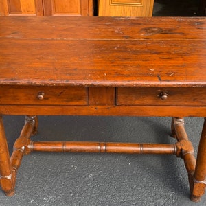 May include: A dark brown wooden table with two drawers and turned legs. The table has a simple design and is in good condition.
