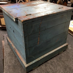 K&ouml;nnte beinhalten: Eine antike blaue Holzkiste mit einem Scharnierdeckel und einem Sockel. Die Kiste hat eine abgenutzte Oberfl&auml;che und ist aus Holzbrettern gefertigt.