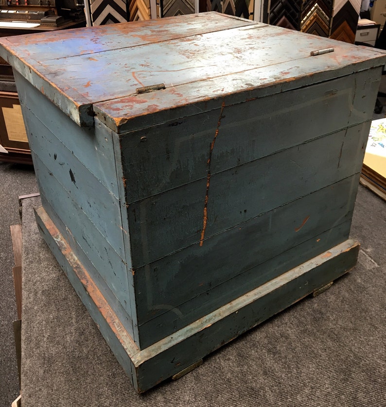 K&ouml;nnte beinhalten: Eine antike blaue Holzkiste mit einem Scharnierdeckel und einem Sockel. Die Kiste hat eine abgenutzte Oberfl&auml;che und ist aus Holzbrettern gefertigt.