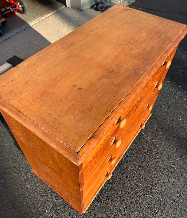 May include: A wooden chest of drawers with five drawers and simple wooden knobs. The chest is a light brown color and has a worn, rustic look.