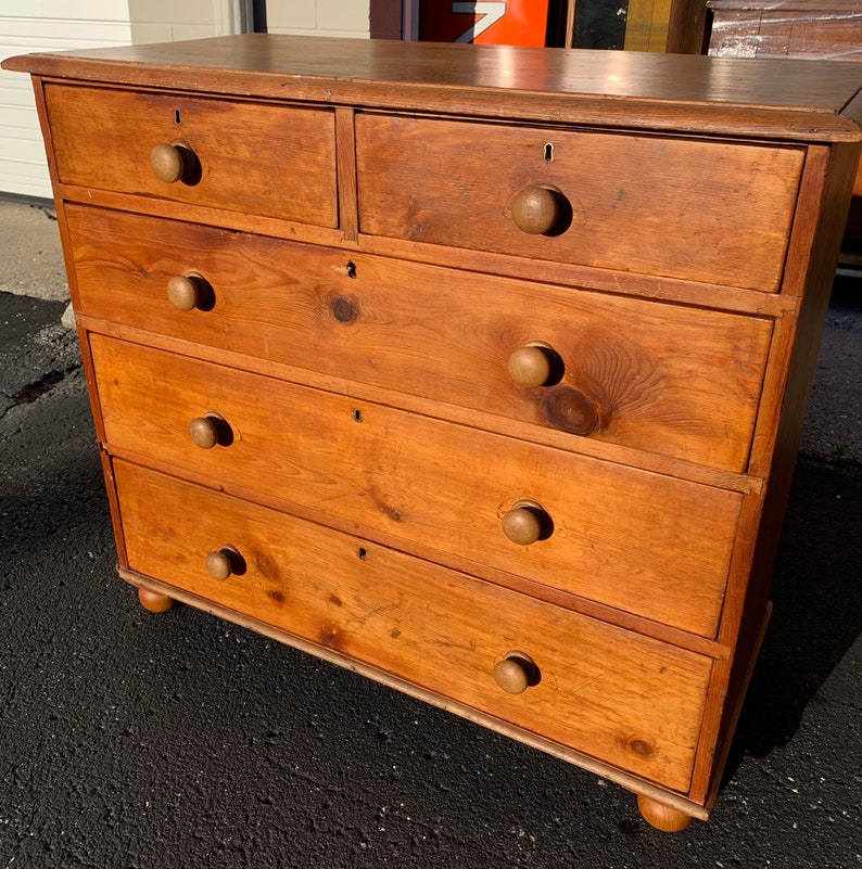 May include: A wooden chest of drawers with five drawers and rounded knobs. The chest of drawers is a light brown color and has a distressed finish.