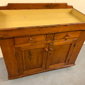 May include: Antique wooden cabinet with a yellow top, two drawers, and two doors. The cabinet has a rustic, farmhouse style.