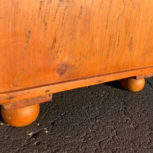 May include: A wooden chest with a natural finish and rounded legs. The chest has a simple design and is made of solid wood.