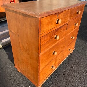 May include: A wooden chest of drawers with five drawers and wooden knobs. The chest of drawers is a light brown color and has a distressed finish.