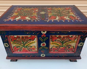May include: A wooden chest with a blue base and red trim. The chest is decorated with hand-painted floral designs in shades of red, yellow, green, and white.