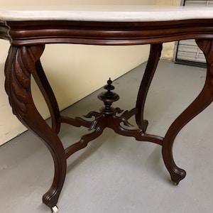 May include: A dark wood table with a white marble top and ornate carved legs. The table has a curved top and a decorative center piece.