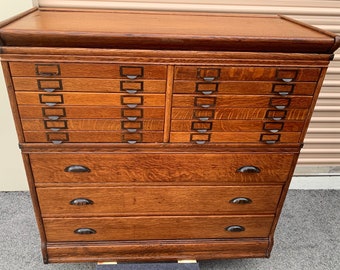 Op de afbeelding: Antiek houten archiefkast met 12 laden en 4 grotere laden. De kast is gemaakt van eikenhout en heeft een donkerbruine afwerking. De laden hebben metalen handgrepen en labels.