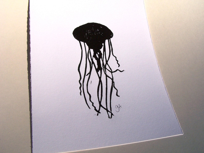 May include: A black and white illustration of a jellyfish. The jellyfish is depicted with a rounded bell and long, flowing tentacles. The artwork is signed with the initials "GA" in the lower right corner. The image is on a white background.