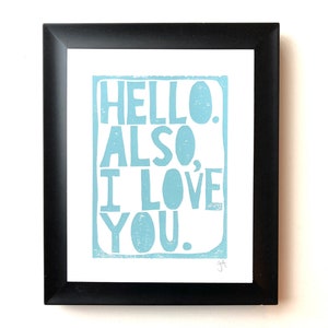 May include: A framed print with the text "HELLO. ALSO. I LOVE YOU." in light blue lettering on a white background.