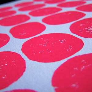 May include: A close-up of a white surface with a repeating pattern of bright pink circles. The circles are slightly textured and appear to be made with paint.