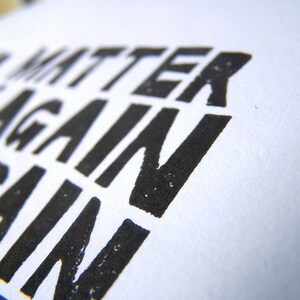 Op de afbeelding: Close-up van een zwart-witte print met de tekst "Het maakt niet uit, probeer het opnieuw".