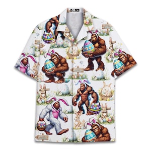 May include: White button-up shirt with a repeating pattern of Bigfoot characters wearing bunny ears and holding Easter eggs and baskets. The design includes Easter eggs, bunnies, and wooden signs on a white background. The shirt has short sleeves.