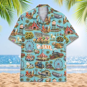 May include: A light blue short-sleeve button-down shirt featuring an all-over print of fairground scenes, farm buildings, animals, and the text AKD. The pattern includes ferris wheels, a steam train, a carousel, and various food items.