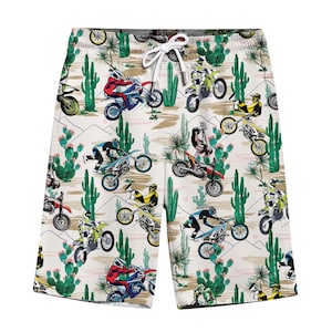 Puede incluir: Pantalones cortos de baño blancos con un estampado repetido de pilotos de motocross, cactus y paisajes desérticos. Los pantalones cortos tienen un cordón y son ideales para la playa o la piscina.