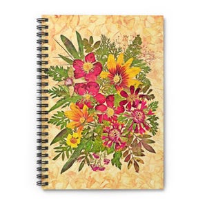 May include: A spiral bound notebook with a pressed flower design on the cover. The flowers are in shades of red, yellow, and orange, and are arranged in a bouquet shape. The background is a light beige colour.