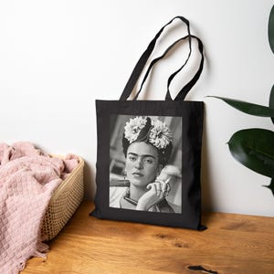Könnte beinhalten: Schwarze und weiße Einkaufstasche mit einem Porträt von Frida Kahlo, die eine Blumenkrone trägt und eine Zigarette hält.